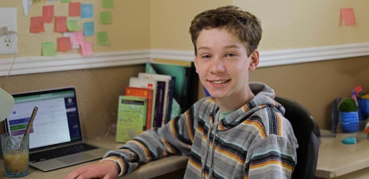 Student smiling at the camera while working with his laptop